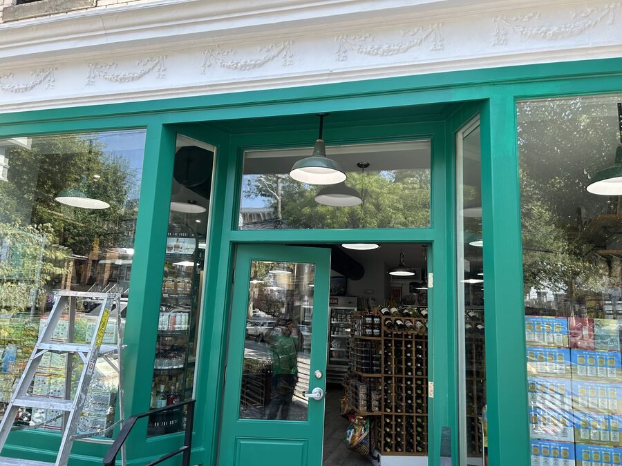Commercial storefront with green doors and ladder during exterior finish work