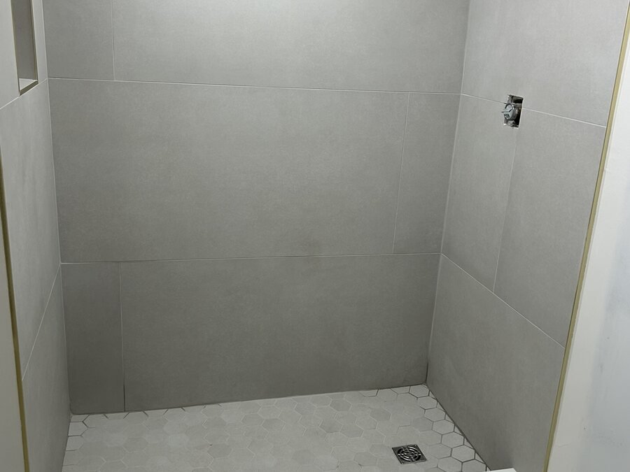 Piso de ducha terminado con azulejo gris y drenaje centrado