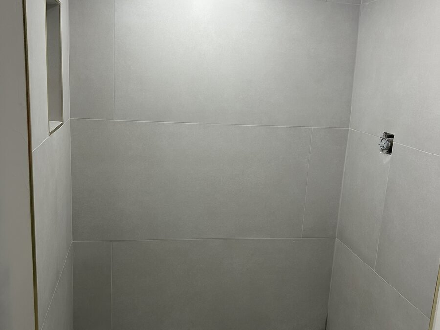 Detalle de pared y piso de ducha con azulejo gris durante el acabado