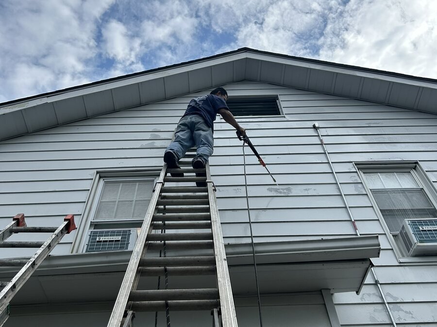 Pintor trabajando desde una escalera en la parte alta de una casa